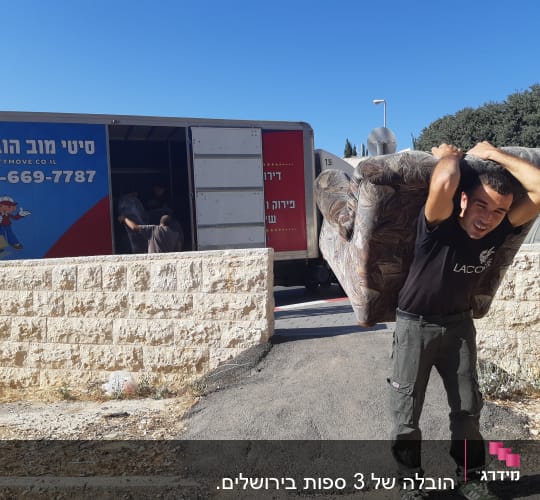 אדם נושא ספה על גבו ליד משאית הובלה